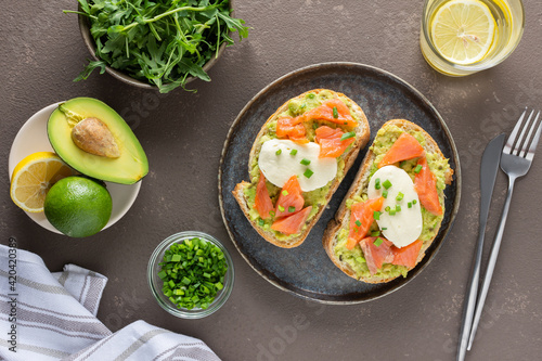 Delicious hearty breakfast, sandwiches with avocado paste, salmon and mozzarella on a plate, arugula and pea sprouts and green onion