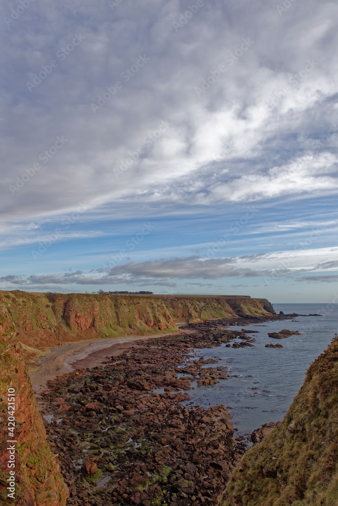 Looking towards Rumness from the headland of Maw Skelly, and the steep red sandstone grass covered Sea Cliffs above a shingle beach.
