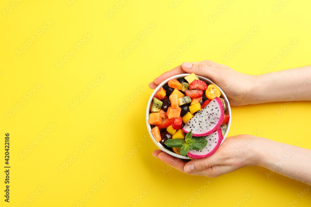 Woman with bowl of delicious exotic fruit salad on yellow background, top view. Space for text Woman with bowl of delicious exotic fruit salad on yellow background, top view. Space for text