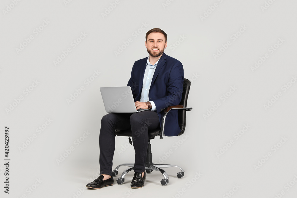 Young businessman with laptop sitting in comfortable office chair on grey background
