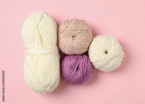 Soft woolen yarns on pink background, flat lay