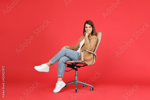 Young woman sitting in comfortable office chair on red background