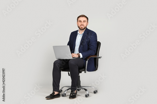 Young businessman with laptop sitting in comfortable office chair on grey background