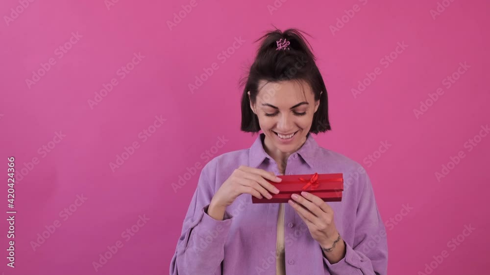 Caucasian woman isolated in casual purple shirt on pink background happy joyful opening red gift box says wow Caucasian woman isolated in casual purple shirt on pink background happy joyful opening red gift box says wow