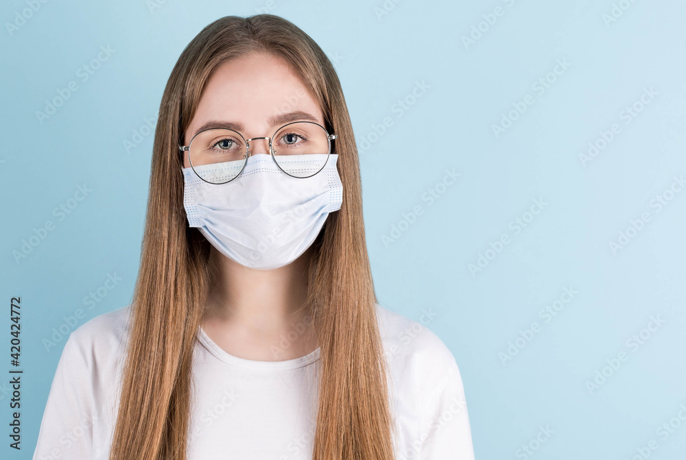 Close-up portrait, she is a cute attractive sweet adorable pin-up girl in glasses, in a white shirt, flu protection, cold face mask, isolated on blue pastel background Close-up portrait, she is a cute attractive sweet adorable pin-up girl in glasses, in a white shirt, flu protection, cold face mask, isolated on blue pastel background