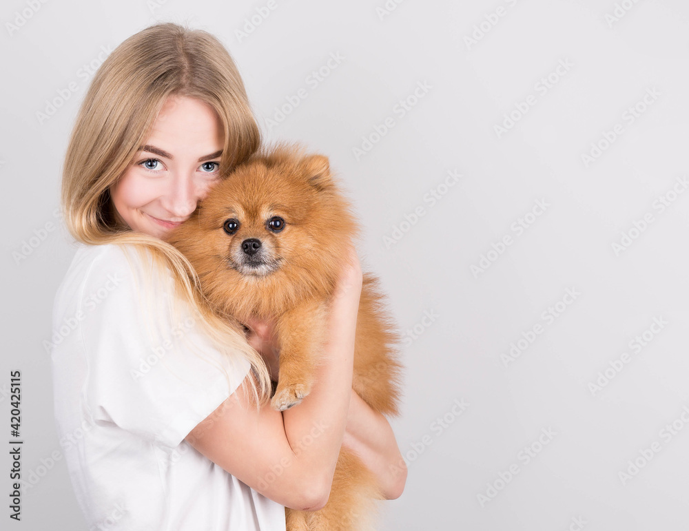 A beautiful blonde young woman hugs and kisses her spitz puppy. Love between dog and owner. Isolated on a gray background. A beautiful blonde young woman hugs and kisses her spitz puppy. Love between dog and owner. Isolated on a gray background.