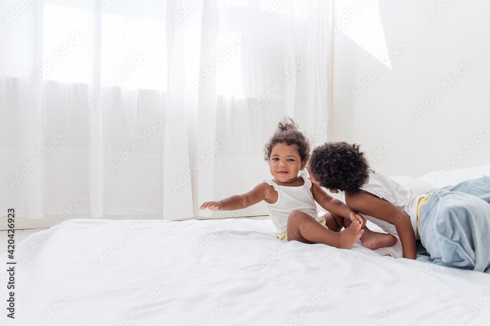 Brother and sister African Americans play together on white bed in loft interior. Siblings having fun among the blue pillows in the morning. Boy kissing little girl on the cheek, caring for a neighbor Brother and sister African Americans play together on white bed in loft interior. Siblings having fun among the blue pillows in the morning. Boy kissing little girl on the cheek, caring for a neighbor
