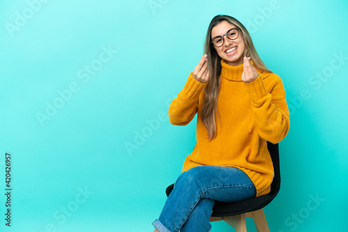 Young caucasian woman sitting on a chair isolated on blue background making money gesture © luismolinero