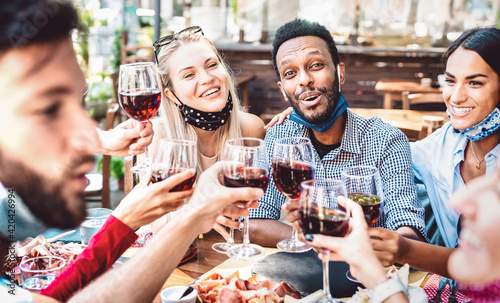 Multiracial people toasting wine at restaurant garden wearing open face mask - New normal lifestyle concept about happy friends having fun together - Bright filter with focus on guy looking at camera
