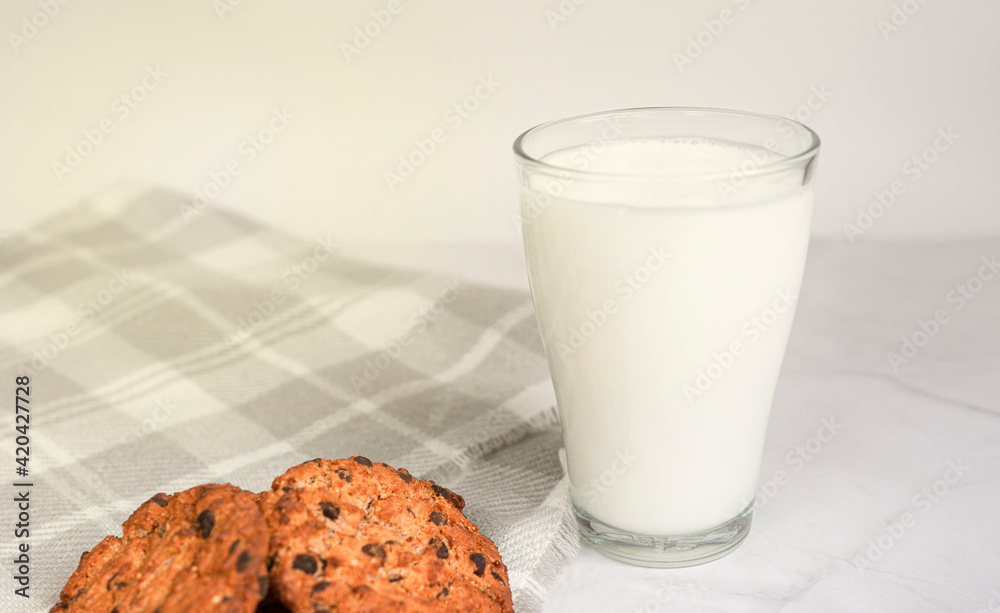 A glass of milk, chocolate oatmeal cookies and crumbs on a white plate in the rays of the sun. Tasty breakfast. The concept of proper nutrition and weight loss. copy space for text A glass of milk, chocolate oatmeal cookies and crumbs on a white plate in the rays of the sun. Tasty breakfast. The concept of proper nutrition and weight loss. copy space for text