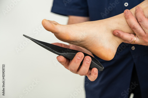 Doctor specializing in plantar posturology in his medical office tests the orthopedic device insoles on the patient's foot - Flatfoot treatment in podiatry clinic photo
