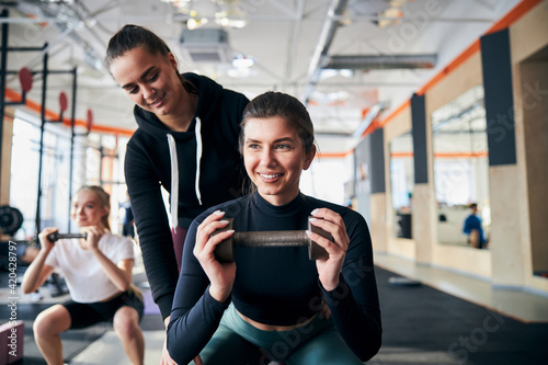 Cheerful young woman squatting with support of her gym partner