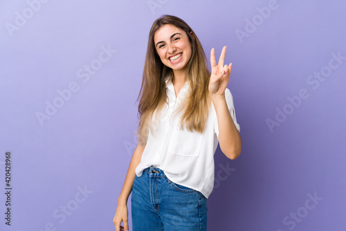 Young woman over isolated purple background smiling and showing victory sign
