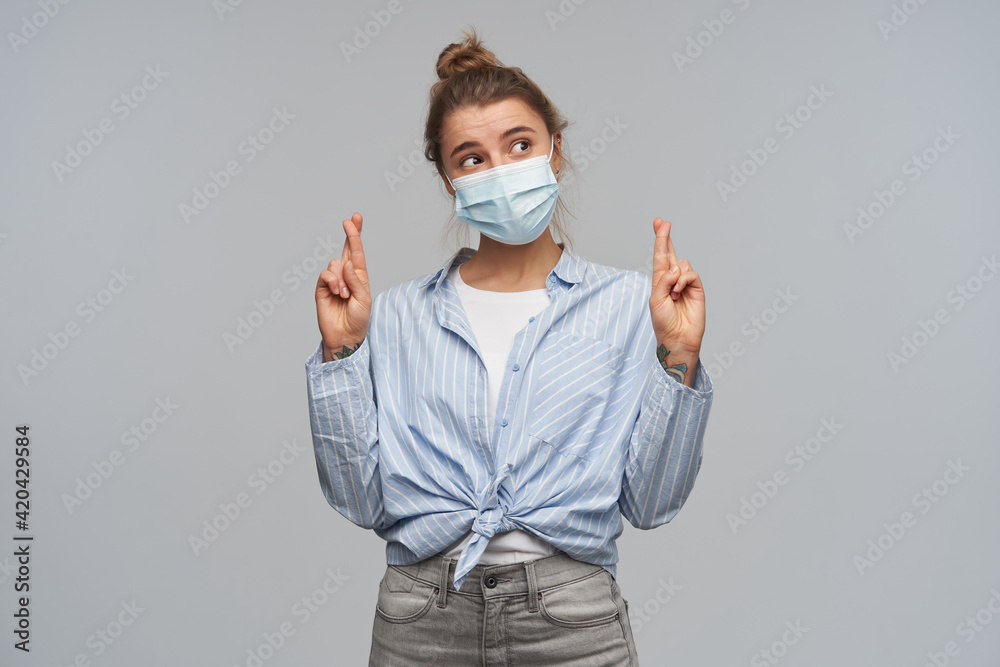 Portrait of dreaming girl with blond hair. Wearing striped knotted shirt and protective face mask. Crossing fingers, making a wish. Watching to the right at copy space, isolated over grey background Portrait of dreaming girl with blond hair. Wearing striped knotted shirt and protective face mask. Crossing fingers, making a wish. Watching to the right at copy space, isolated over grey background