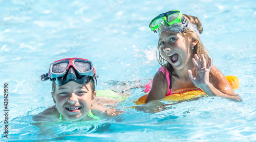 Two female kids having fun inside the pool on a summer day wearing swimming goggles on their foreheads © weyo