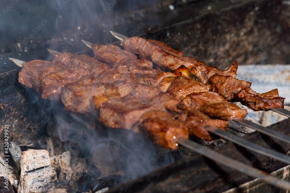 beef kebab is fumbled over coals in smoke. juicy barbecue beef steaks are cooked in a restaurant over an open fire beef kebab is fumbled over coals in smoke. juicy barbecue beef steaks are cooked in a restaurant over an open fire