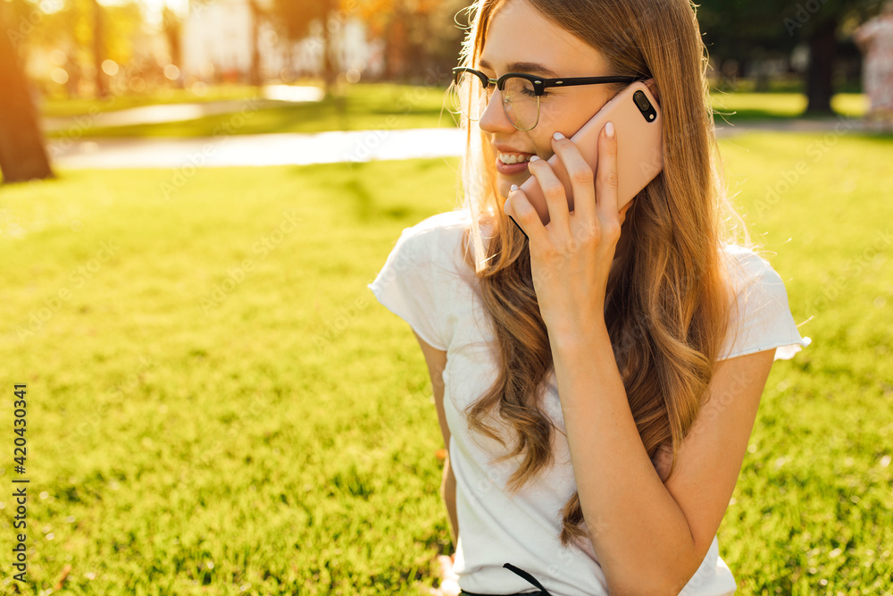 Young woman talking on the phone while sitting in the park on a green lawn Young woman talking on the phone while sitting in the park on a green lawn
