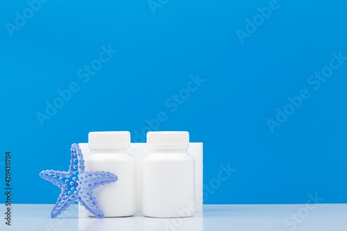 Two medication bottles with sea star against blue background with copy space. Supplements with sea minerals for healthy living. Concept of wellness, vitamins and supplements