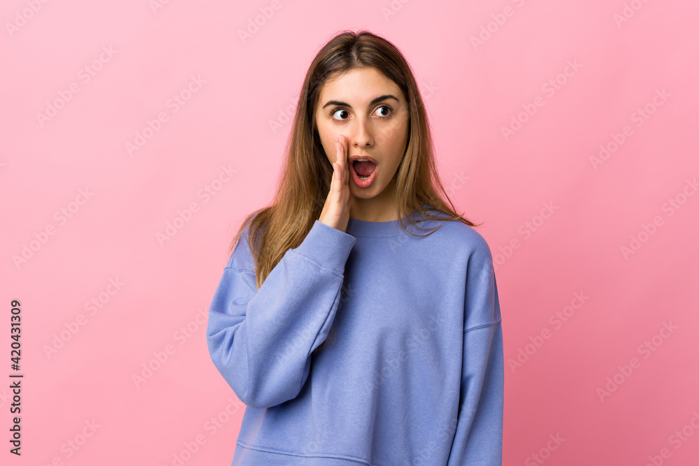 Fototapeta premium Young woman over isolated pink background whispering something with surprise gesture while looking to the side