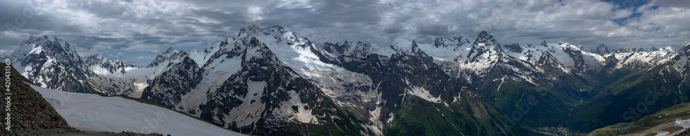 Wide panorama of the mountain peaks of the Caucasian ridge in cloudy weather