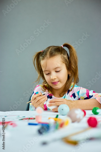 Happy little girl painting, drawing with brush eggs at home.