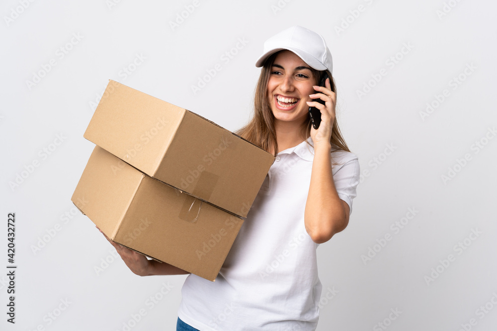 Young delivery woman over isolated white background keeping a conversation with the mobile phone with someone