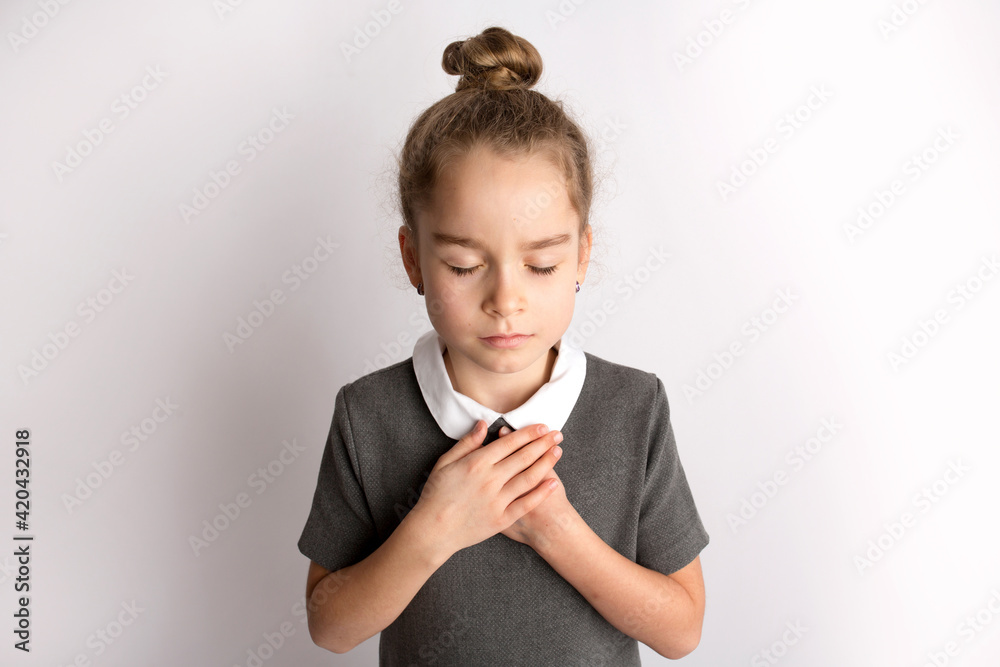 Attractive little girl in a strict school dress, stands on a white background with empty copy space, gestures with her hands, admires a happy expression on her face Attractive little girl in a strict school dress, stands on a white background with empty copy space, gestures with her hands, admires a happy expression on her face
