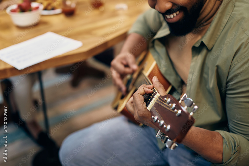 Close-up of black man playing acoustic guitar at home.