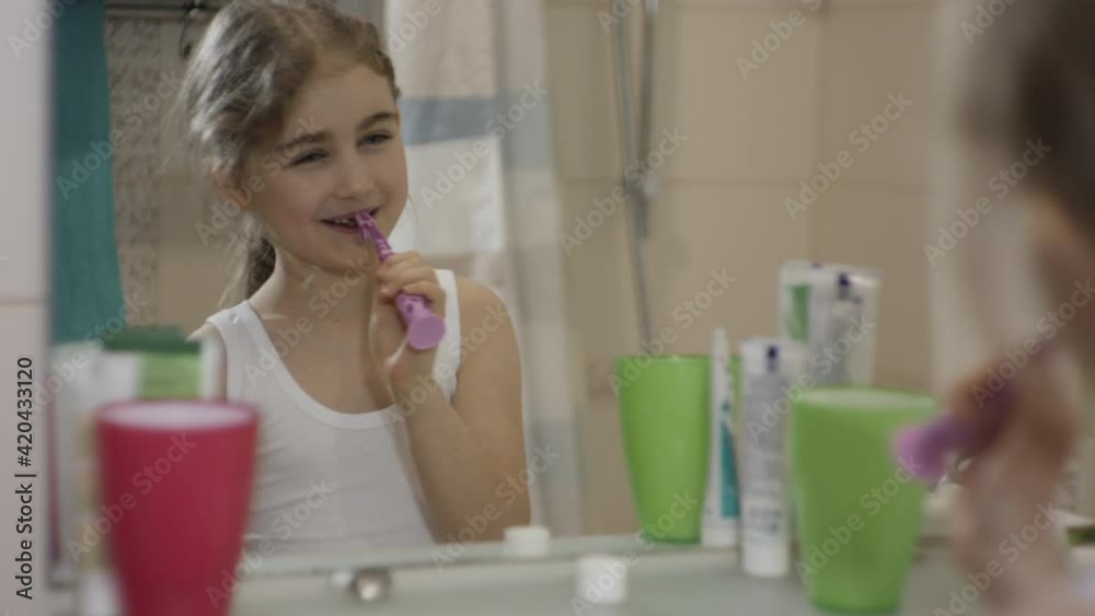 Close-up Portrait Young Little Girl Dancing Singing With Toothbrush in Bathroom Looking at Mirror Reflection. Daily Routine Dental Hygiene. Happy Portrait Caucasian Toothless Child Dancing in Bathroom Close-up Portrait Young Little Girl Dancing Singing With Toothbrush in Bathroom Looking at Mirror Reflection. Daily Routine Dental Hygiene. Happy Portrait Caucasian Toothless Child Dancing in Bathroom