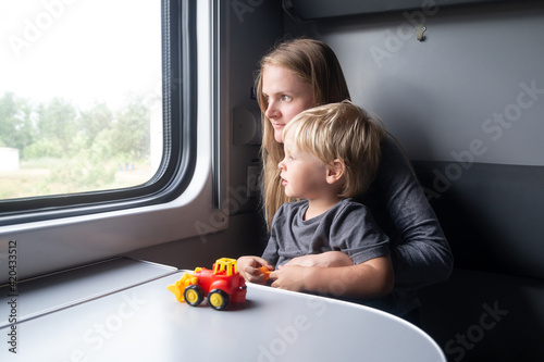 Woman with kid in a train compartment looks out the window. Family travel in the train cabin