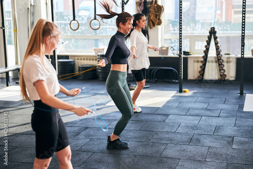 Excited young ladies staying in shape and using skipping ropes