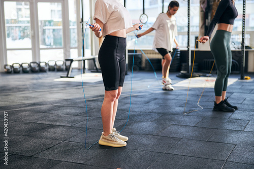 Slender young women skipping with ropes at gym