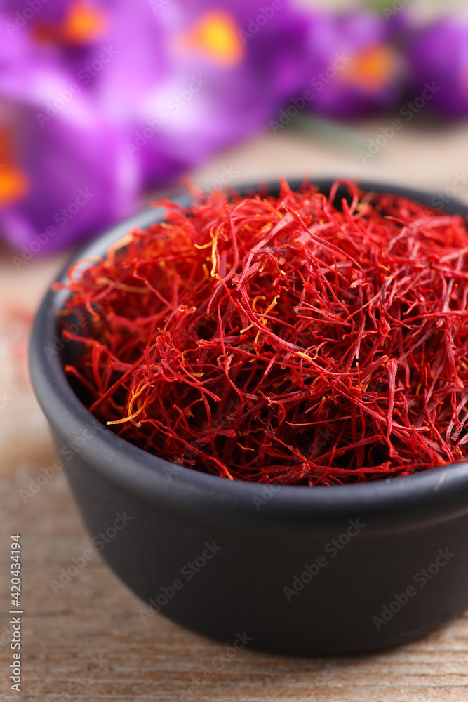 Fototapeta premium Dried saffron in bowl and crocus flowers on wooden table, closeup