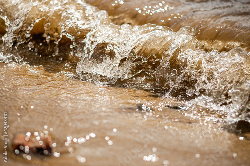Waves with bright splashes of river water on a sandy beach on a sunny day