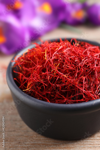 Dried saffron in bowl and crocus flowers on wooden table, closeup