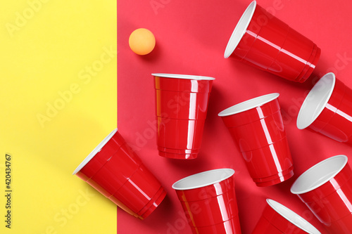 Plastic cups and ball on color background, flat lay. Beer pong game