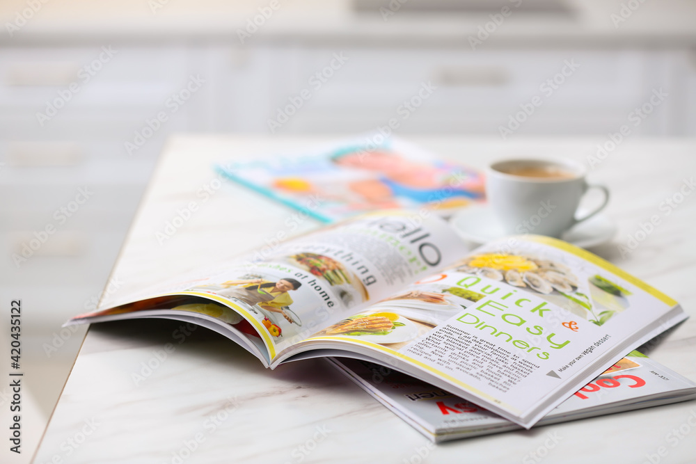 Naklejka premium Culinary magazines and cup of coffee on table in kitchen