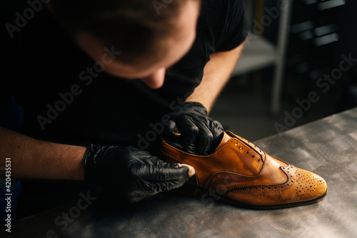 Top close-up view of professional shoemaker wearing black gloves polishing old light brown leather shoes. Concept of cobbler artisan repairing and restoration work in shoe repair shop. photo