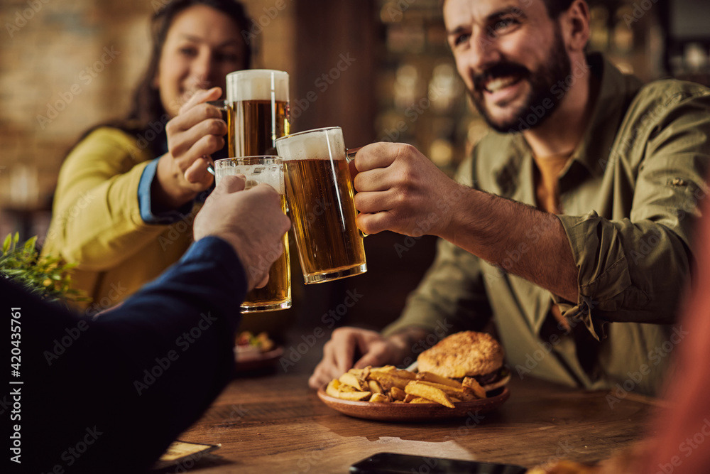 Close-up of friends toasting with beer in a bar.