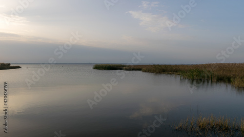 view of the lake before sunset, sunbeams through the clouds, calm water surface, lake meadow foreground © ANDA