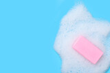 A piece of soap with foam on blue background. Backdrop with space for your text. Top view.