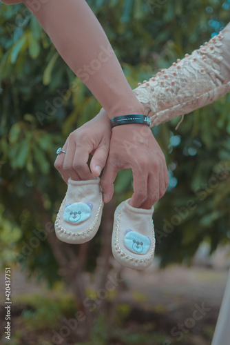 man and pregnant women wearing couple shirt holding white baby shoes, family love concept