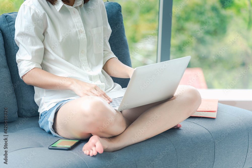Naklejka premium Woman working from home on laptop online meeting in home office. Entrepreneur asian business woman using notebook laptop sit on sofa technology new normal lifestyle. Happy woman typing keyboard laptop