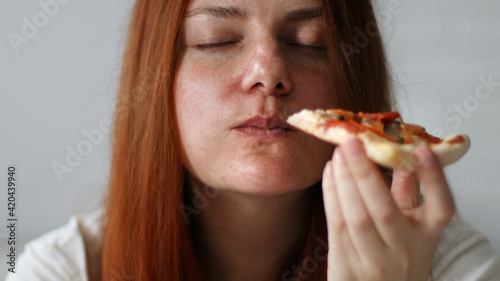 Young  chubby woman with long hair holding tasty big slice of pizza ready to eat at home
