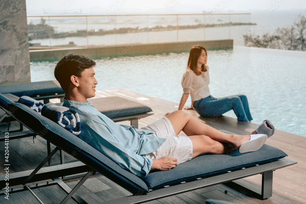 Asian couple sitting near pool with perfect sea view.Summer,Vacation,Love couple and sweet couple concept. Asian couple sitting near pool with perfect sea view.Summer,Vacation,Love couple and sweet couple concept.