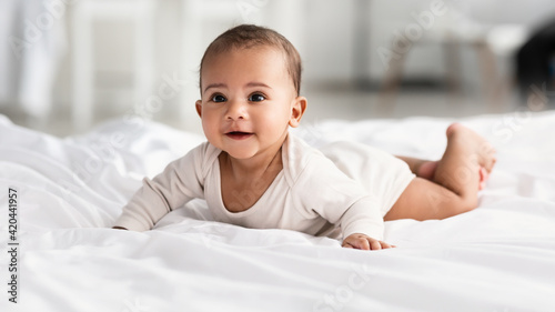 Cute little African American infant lying on white bed