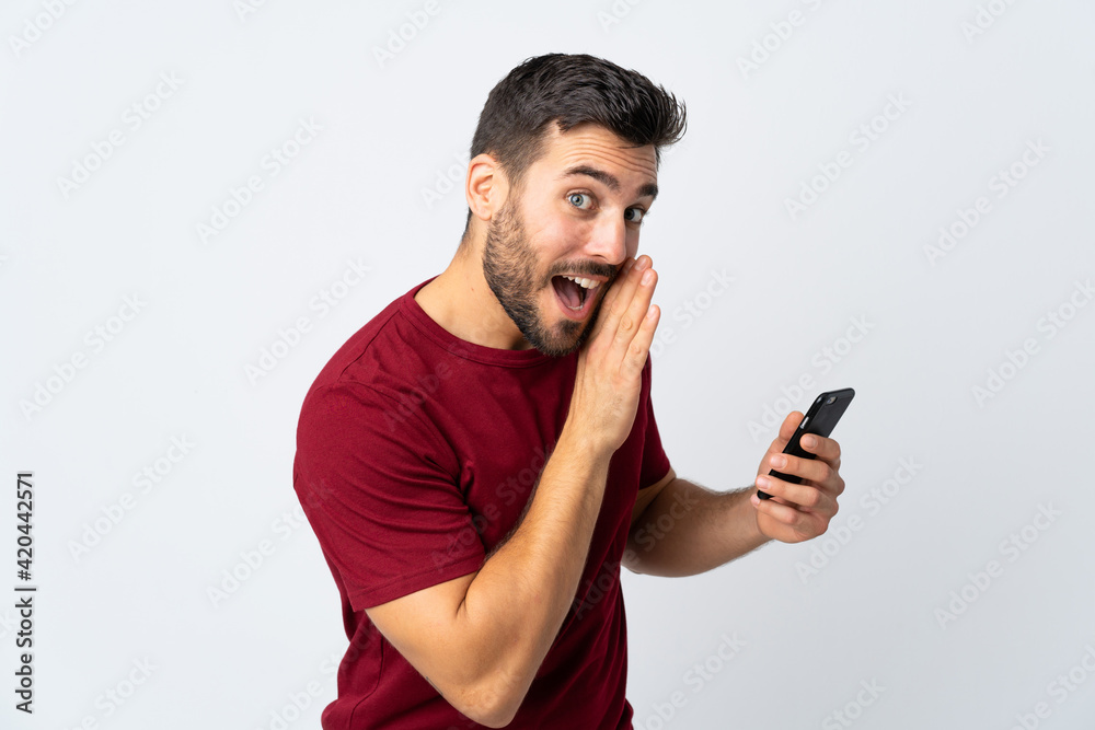 Young handsome man with beard using mobile phone isolated on white background whispering something Young handsome man with beard using mobile phone isolated on white background whispering something