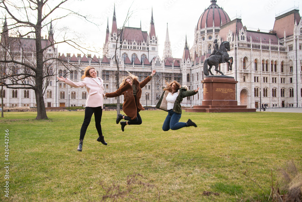 Fototapeta premium Travel to Hungary, European tour. Tourists - Girls and a guy near the Hungarian parliament. A group of people are traveling across Europe.