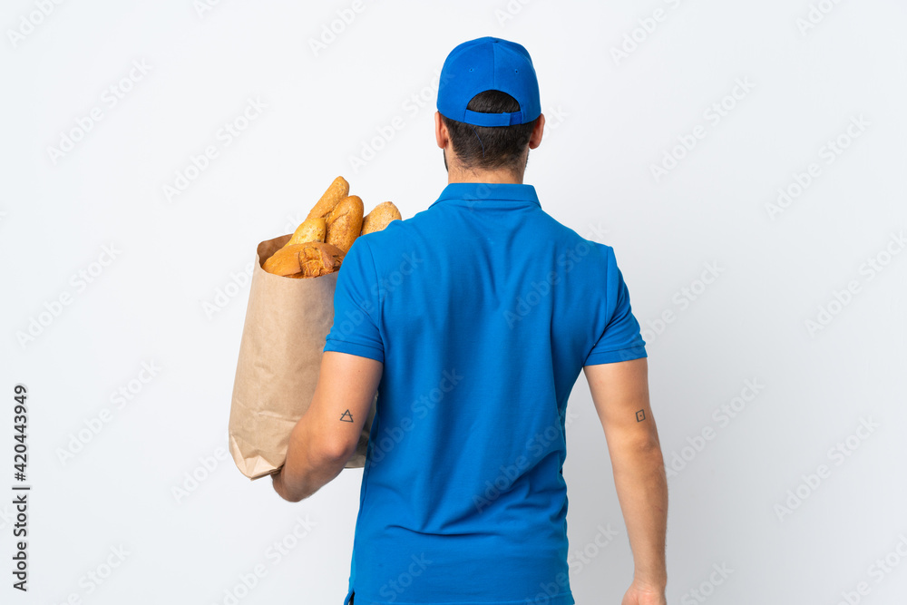 Delivery man holding a bag full of breads isolated on white background in back position