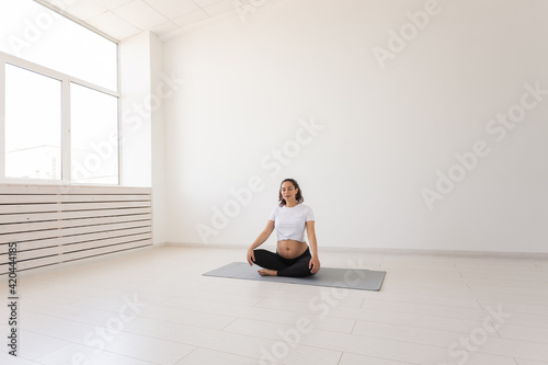 Healthy beautiful pregnant woman meditates before yoga class and relaxes while sitting on mat on the floor. Concept of physical and mental preparation of body for childbirth. Copyspace